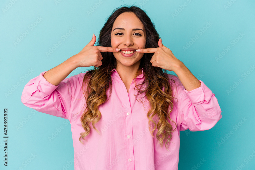 Young mexican woman isolated on blue background smiles, pointing fingers at mouth. Young mexican woman isolated on blue background smiles, pointing fingers at mouth.