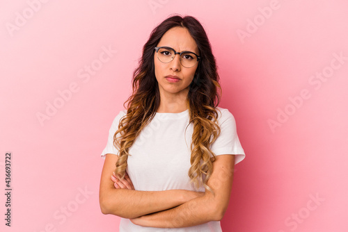 Young mexican woman isolated on pink background frowning face in displeasure, keeps arms folded.