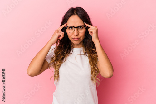 Young mexican woman isolated on pink background focused on a task, keeping forefingers pointing head. © Asier