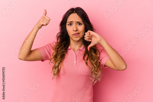Young mexican woman isolated on pink background showing thumbs up and thumbs down, difficult choose concept