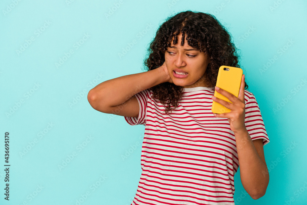 Young mixed race woman holding a mobile phone isolated on blue background touching back of head, thinking and making a choice.