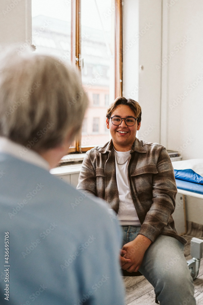 Smiling male patient looking at senior female medical expert during consultation in clinic Smiling male patient looking at senior female medical expert during consultation in clinic