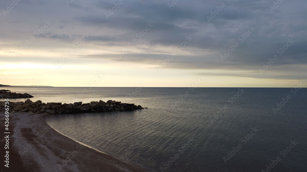 Aerial view of the coastline with beach and water surface to the horizon with orange sunset reflexes for a natural background Aerial view of the coastline with beach and water surface to the horizon with orange sunset reflexes for a natural background