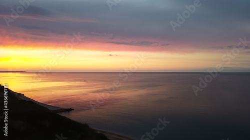 Aerial view of the high shore, the sky with yellow-red stripes from the setting sun, and the sea with yellow-red reflexes on the water as a natural background