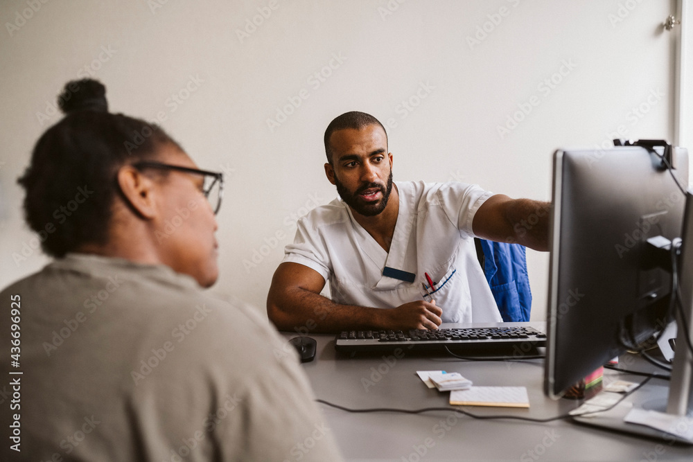 Male healthcare worker discussing over computer with female patient in medical clinic Male healthcare worker discussing over computer with female patient in medical clinic
