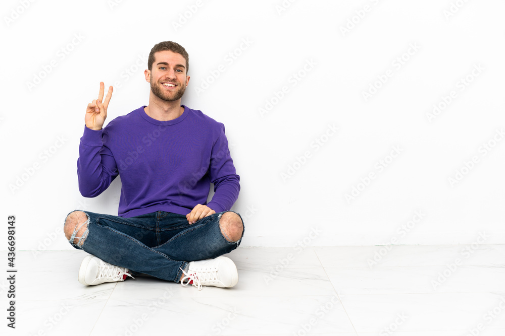 Young man sitting on the floor smiling and showing victory sign