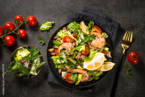 Seafood salad with fresh leaves tomatoes and fried seafood. Top view at black stone table.