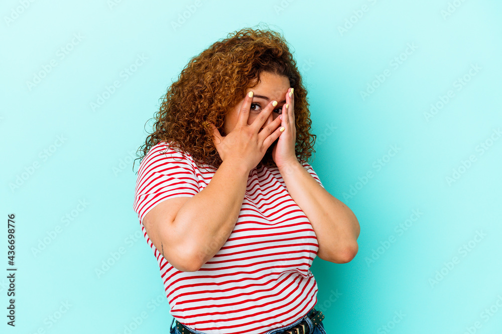 Young latin curvy woman isolated on blue background blink through fingers frightened and nervous. Young latin curvy woman isolated on blue background blink through fingers frightened and nervous.