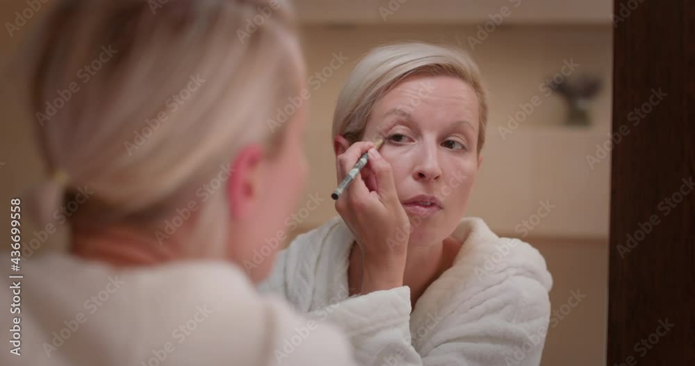 Woman looking in the mirror, underlines her eye by brush with eye shadows Woman looking in the mirror, underlines her eye by brush with eye shadows