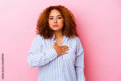 Young latin curvy woman isolated on pink background taking an oath, putting hand on chest.