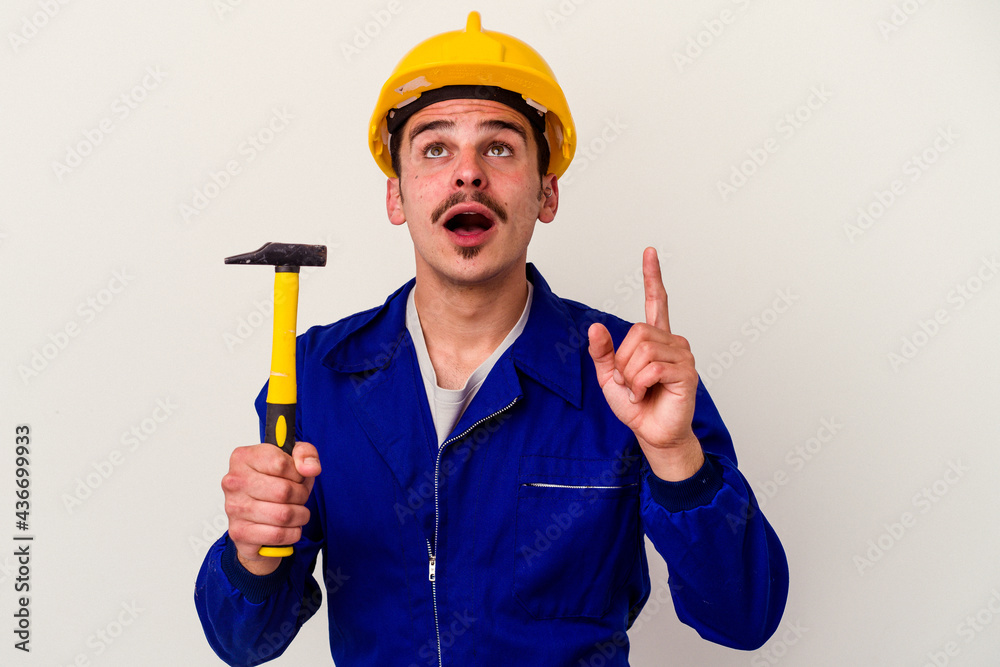 Young caucasian worker man holding a hammer isolated on white background pointing upside with opened mouth.