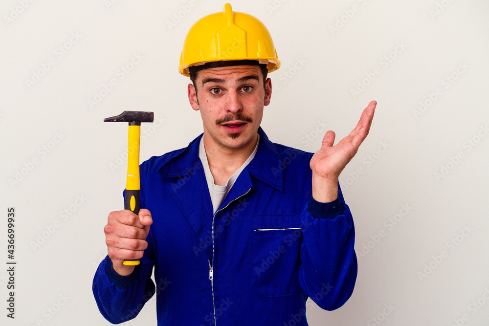 Young caucasian worker man holding a hammer isolated on white background surprised and shocked.