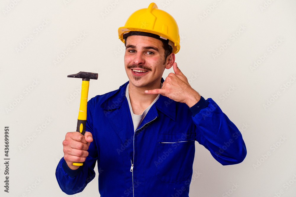 Young caucasian worker man holding a hammer isolated on white background showing a mobile phone call gesture with fingers.