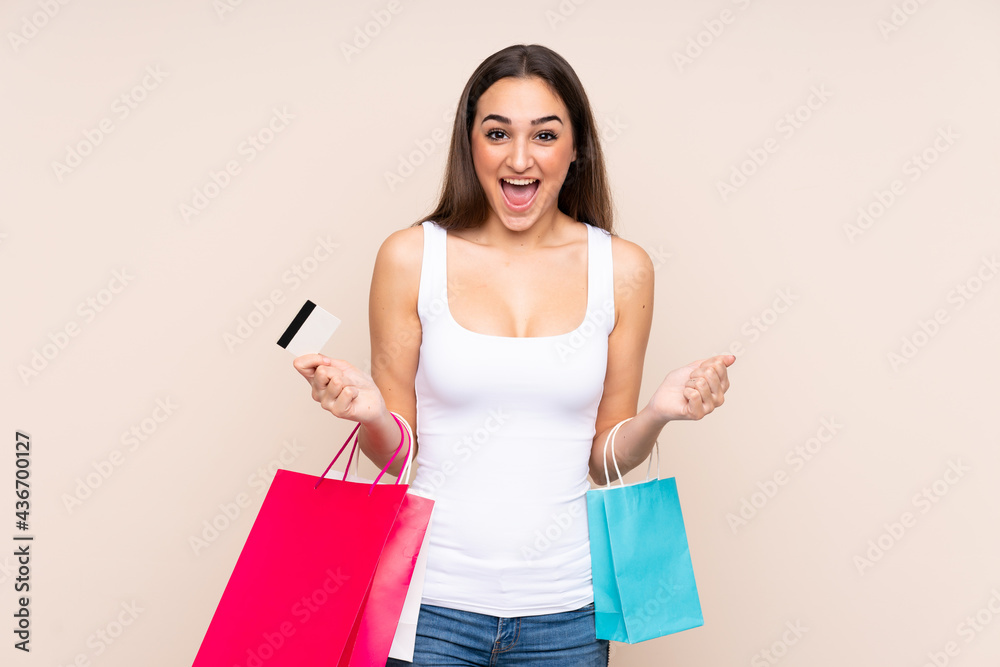 Young caucasian woman isolated on beige background holding shopping bags and surprised