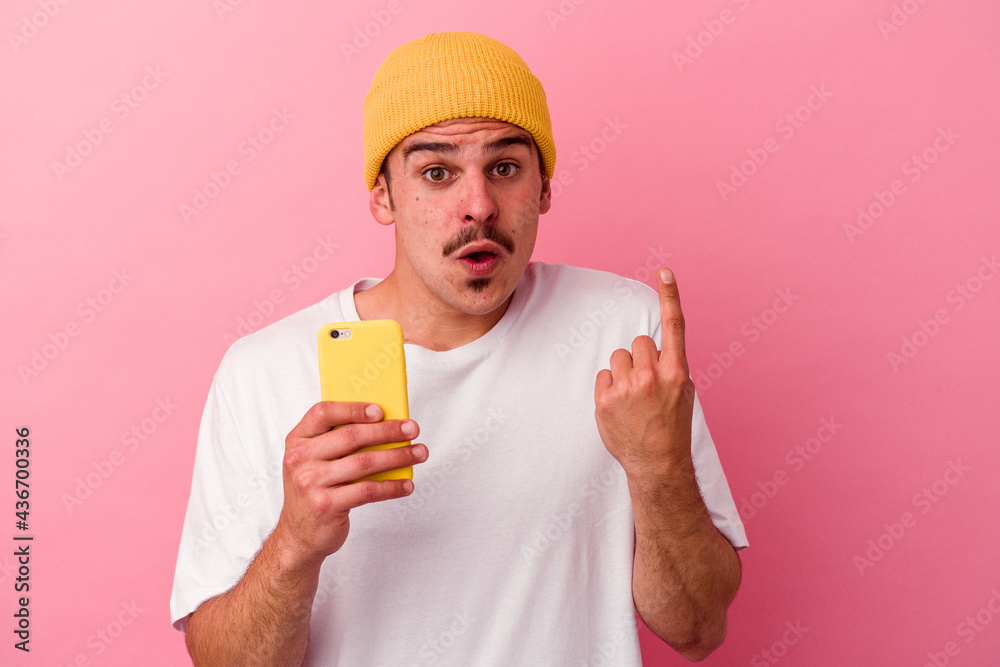 Young caucasian man holding a mobile phone isolated on pink background having some great idea, concept of creativity. Young caucasian man holding a mobile phone isolated on pink background having some great idea, concept of creativity.