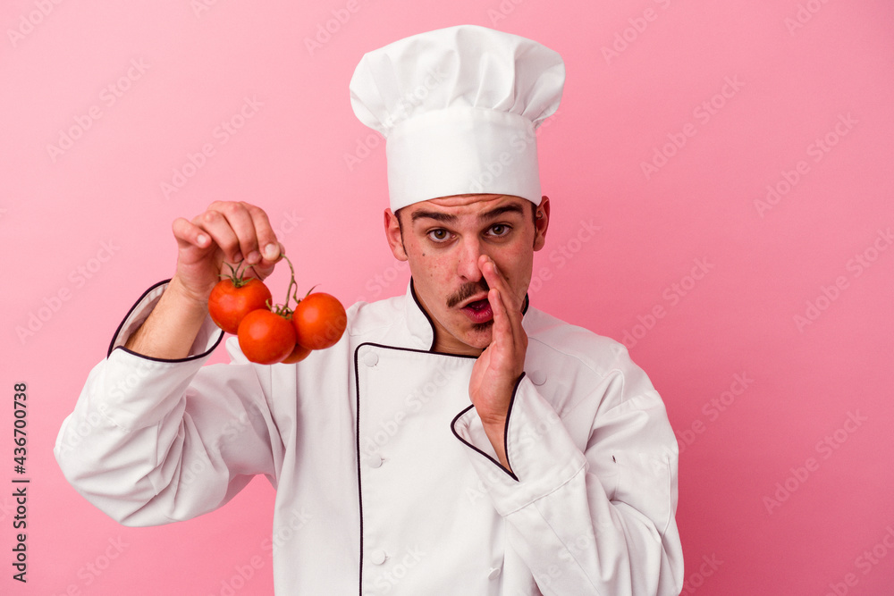Young caucasian chef man holding tomatoes isolated on pink background is saying a secret hot braking news and looking aside Young caucasian chef man holding tomatoes isolated on pink background is saying a secret hot braking news and looking aside