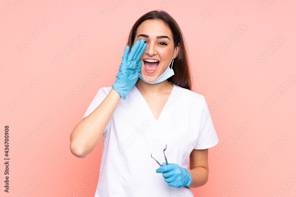 Woman dentist holding tools isolated on pink background shouting with mouth wide open Woman dentist holding tools isolated on pink background shouting with mouth wide open
