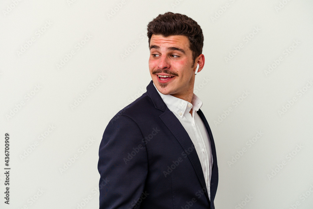 Young business caucasian man wearing wireless headphones isolated on white background looks aside smiling, cheerful and pleasant. Young business caucasian man wearing wireless headphones isolated on white background looks aside smiling, cheerful and pleasant.
