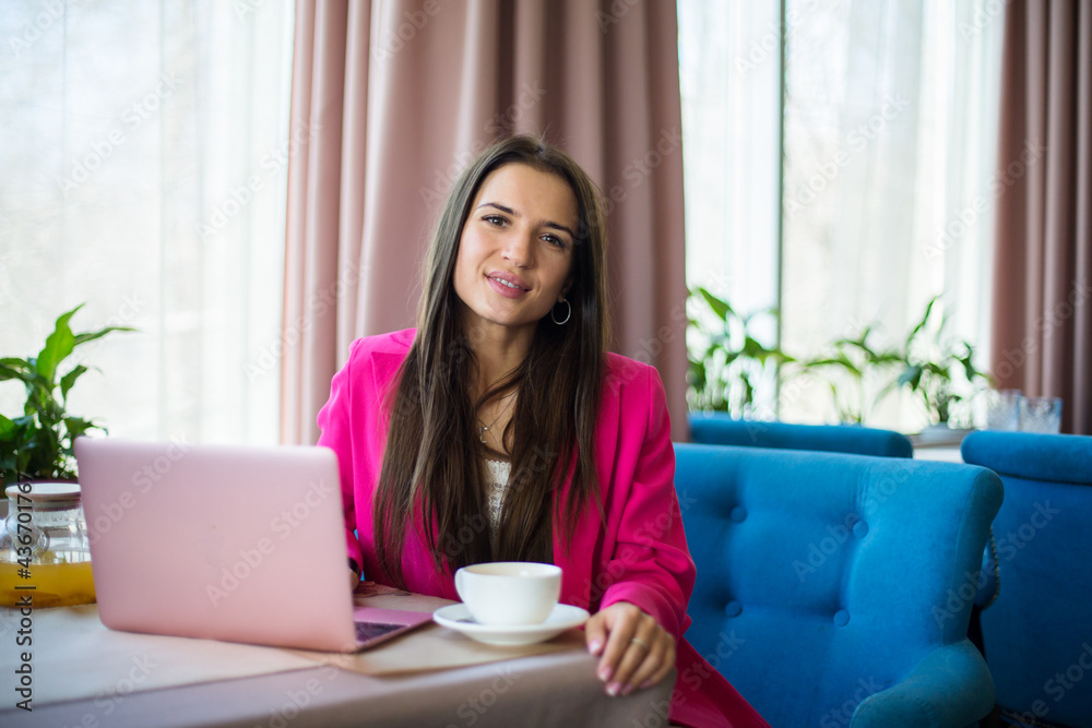young female in crimson suit sit at the table with cup off tea and laptop in the restaurant young female in crimson suit sit at the table with cup off tea and laptop in the restaurant