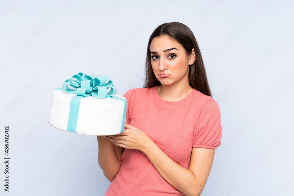 Pastry chef holding a big cake isolated on blue background Pastry chef holding a big cake isolated on blue background