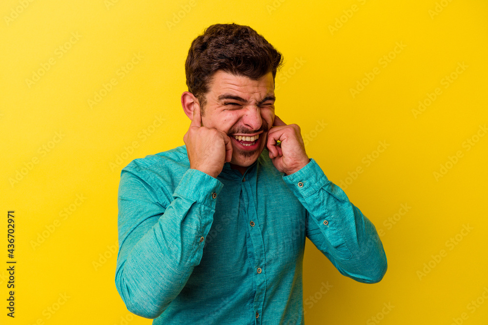 Young caucasian man isolated on yellow background covering ears with hands. Young caucasian man isolated on yellow background covering ears with hands.