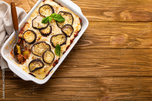 Greek mediterranean dish Moussaka with baked eggplants, ground beef in white ceramic casserole with napkin on wooden rustic background from above, traditional dish of Greece