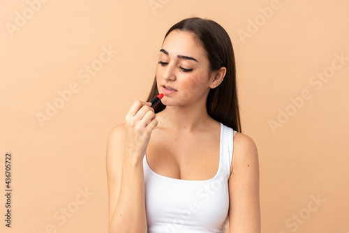Young caucasian woman isolated on beige background holding red lipstick