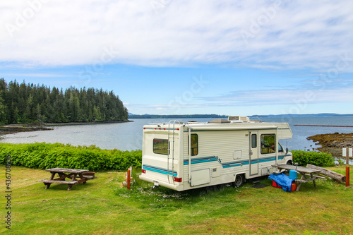 Vacation - holiday in the campground. The view on the picnic table and the white RV parked on the shore in Alder Bay. The beautiful view on the ocean and woods. 