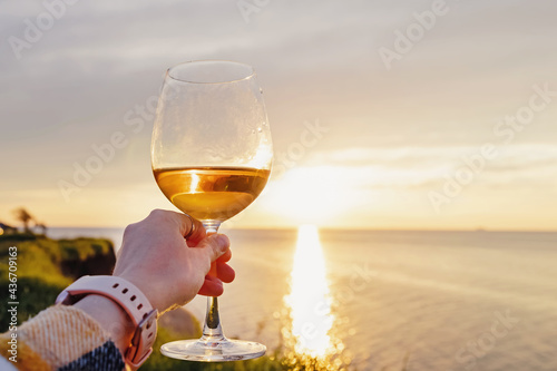 Woman hand holding a glass of rose wine at sunset photo