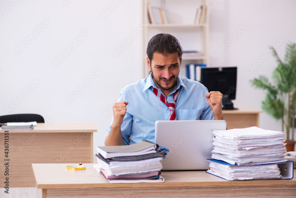 Young male employee unhappy with excessive work in the office Young male employee unhappy with excessive work in the office