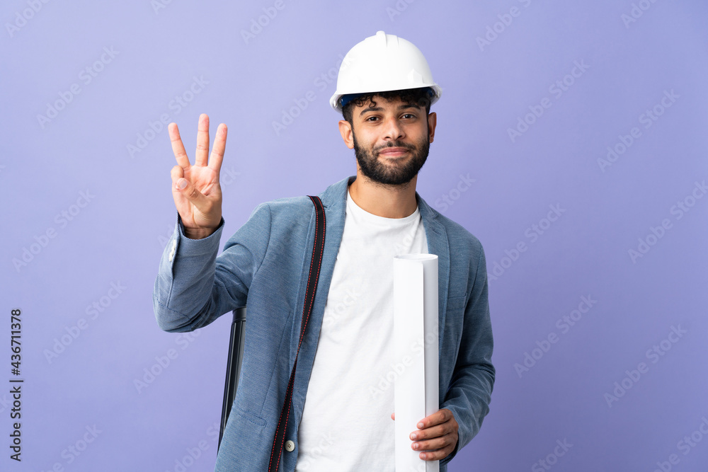 Young architect Moroccan man with helmet and holding blueprints over isolated background happy and counting three with fingers Young architect Moroccan man with helmet and holding blueprints over isolated background happy and counting three with fingers
