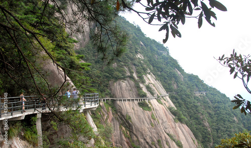 Sanqingshan Mountain in Jiangxi Province, China. People walking along a path clinging to the cliff high up on Mount Sanqing. Sanqingshan is a Taoist mountain famous for its peaks and forests. photo