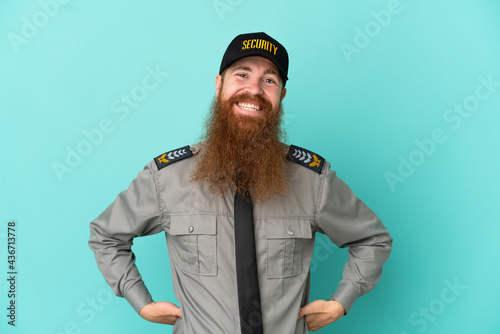 Redhead security man isolated on white background posing with arms at hip and smiling