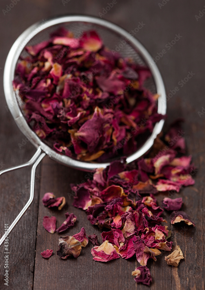 Rose petals organic aroma tea in strainer infuser on wooden background.
