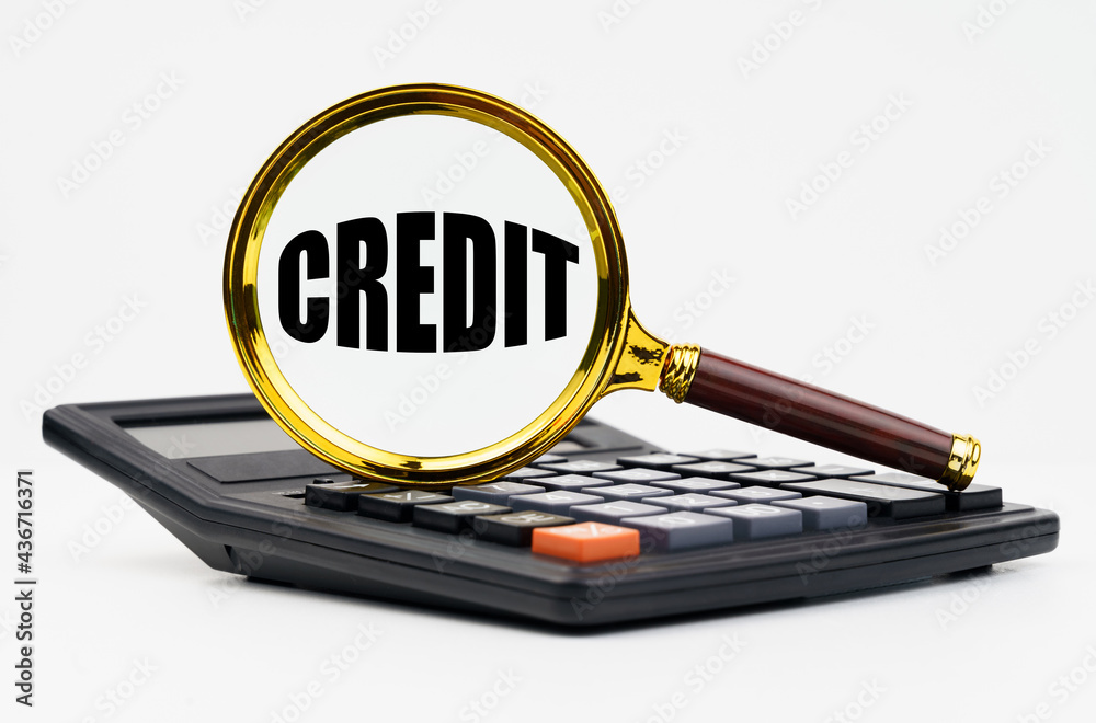 On a white background lies a calculator and a magnifying glass with the inscription - CREDIT On a white background lies a calculator and a magnifying glass with the inscription - CREDIT