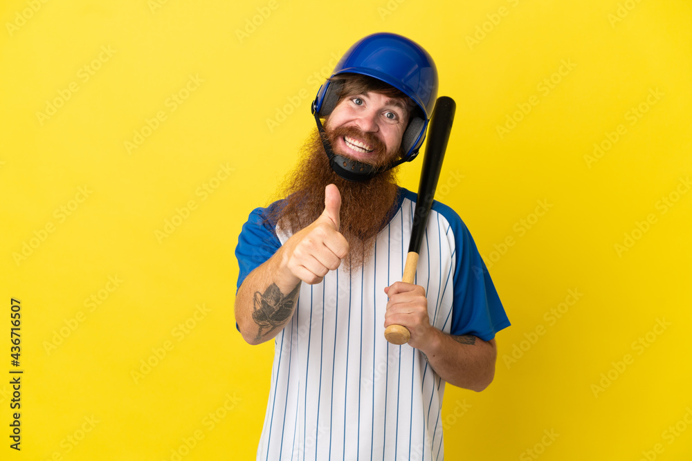 Redhead baseball player man with helmet and bat isolated on yellow background giving a thumbs up gesture Redhead baseball player man with helmet and bat isolated on yellow background giving a thumbs up gesture