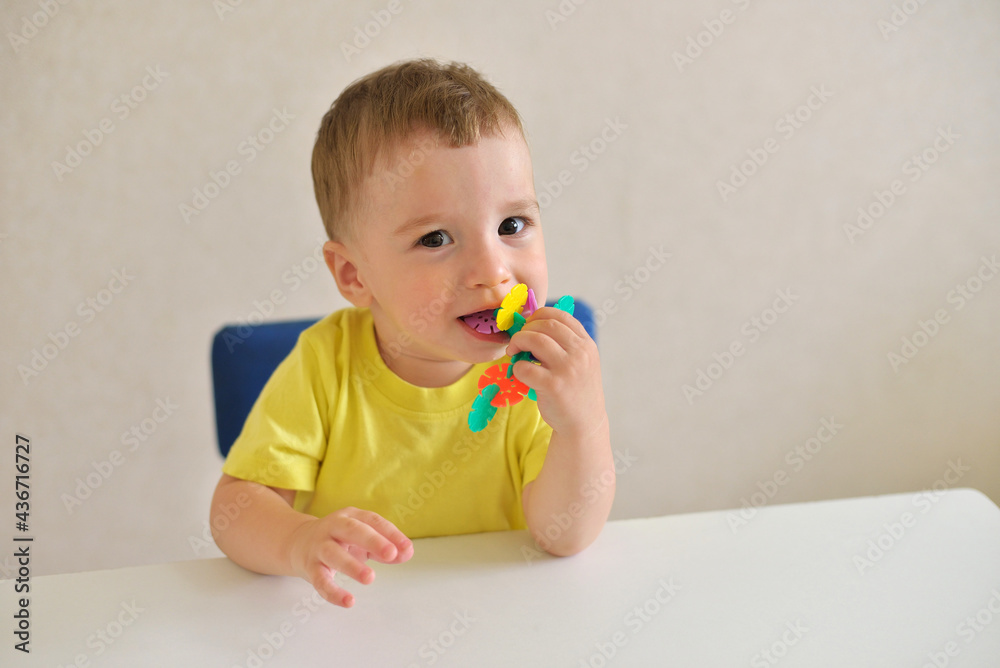 toddler boy plays constructor while sitting at a white table. educational game Montessori fine motor skills. early development concept. takes dangerous toys in his mouth toddler boy plays constructor while sitting at a white table. educational game Montessori fine motor skills. early development concept. takes dangerous toys in his mouth