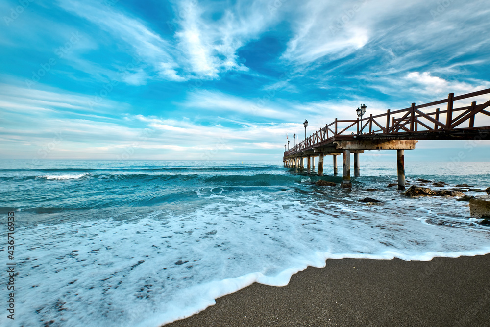View of sandy beach and a wooden pier on the Costa del Sol in the resort town of Marbella in Spain
