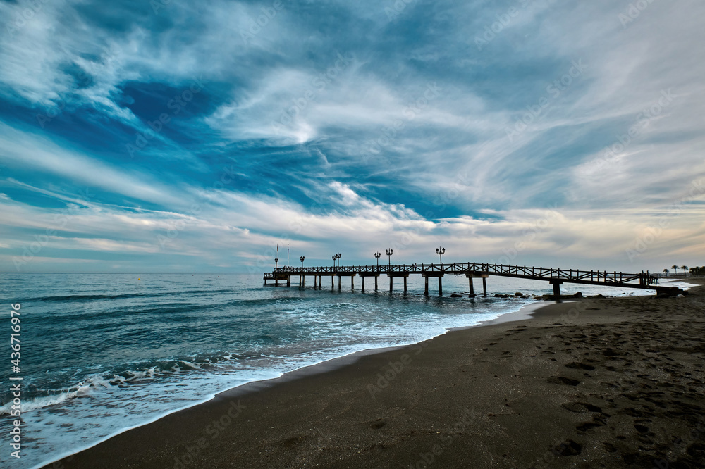 Sandy beach and a wooden pier on Costa del Sol in resort city of Marbella in Spain