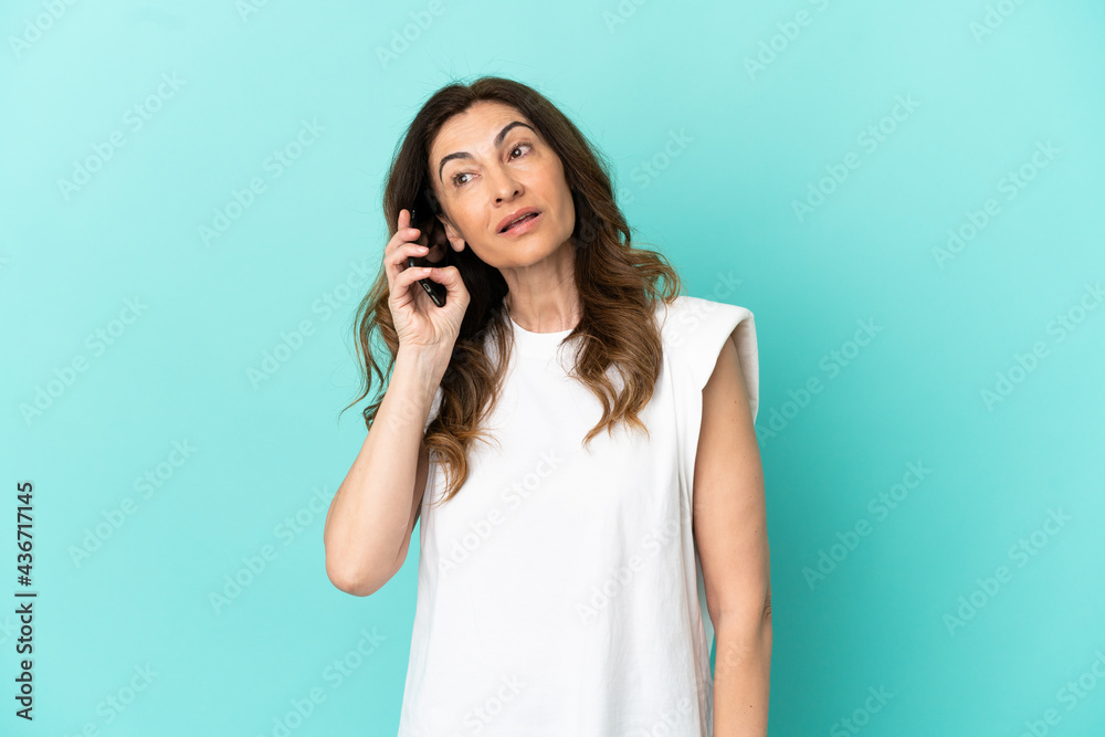 Middle aged caucasian woman isolated on blue background keeping a conversation with the mobile phone Middle aged caucasian woman isolated on blue background keeping a conversation with the mobile phone