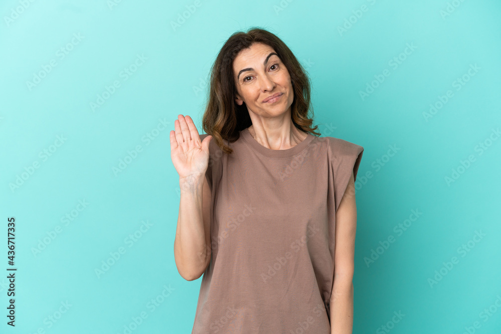 Middle aged caucasian woman isolated on blue background saluting with hand with happy expression Middle aged caucasian woman isolated on blue background saluting with hand with happy expression