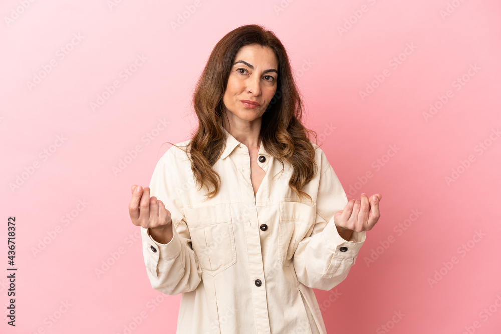 Middle aged caucasian woman isolated on pink background making money gesture Middle aged caucasian woman isolated on pink background making money gesture