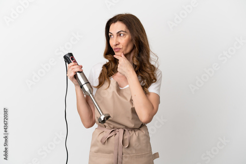 Middle aged caucasian woman using hand blender isolated on white background looking to the side and smiling