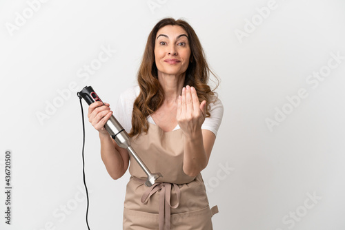 Middle aged caucasian woman using hand blender isolated on white background inviting to come with hand. Happy that you came
