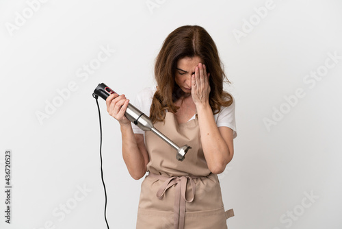 Middle aged caucasian woman using hand blender isolated on white background with tired and sick expression
