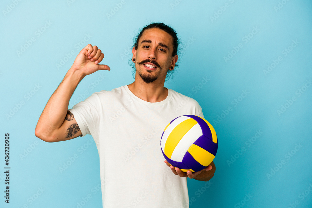 Young caucasian man with long hair isolated on blue background feels proud and self confident, example to follow.