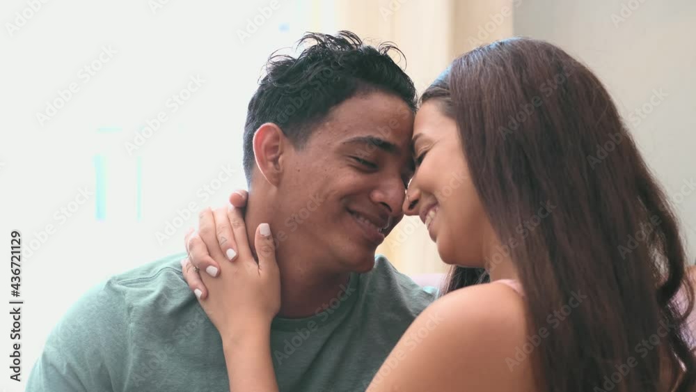 Young millennial interracial couple hug with love at home in living room - relationship with black boy and caucasian girl together standing and embracing looking each other - concept of life and house