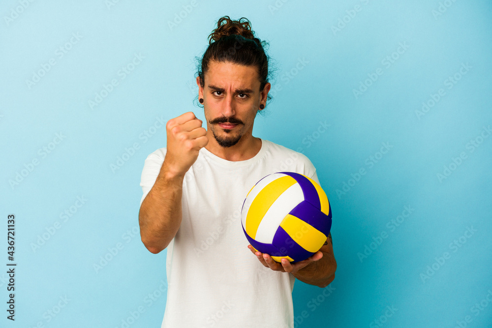 Young caucasian man with long hair isolated on blue background showing fist to camera, aggressive facial expression.