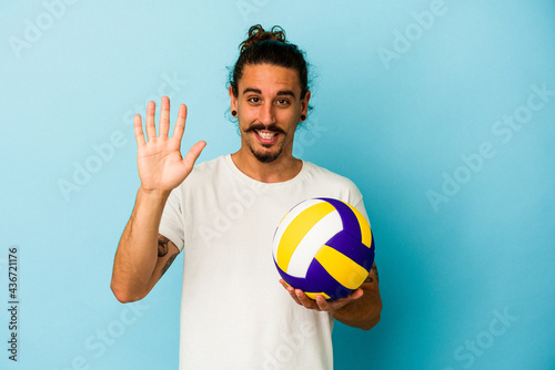 Young caucasian man with long hair isolated on blue background smiling cheerful showing number five with fingers.