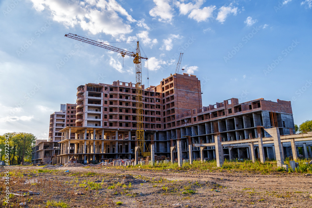 Tall building under construction with scaffolds,Freestanding tower crane on a building site.Building construction site work against blue sky Tall building under construction with scaffolds,Freestanding tower crane on a building site.Building construction site work against blue sky